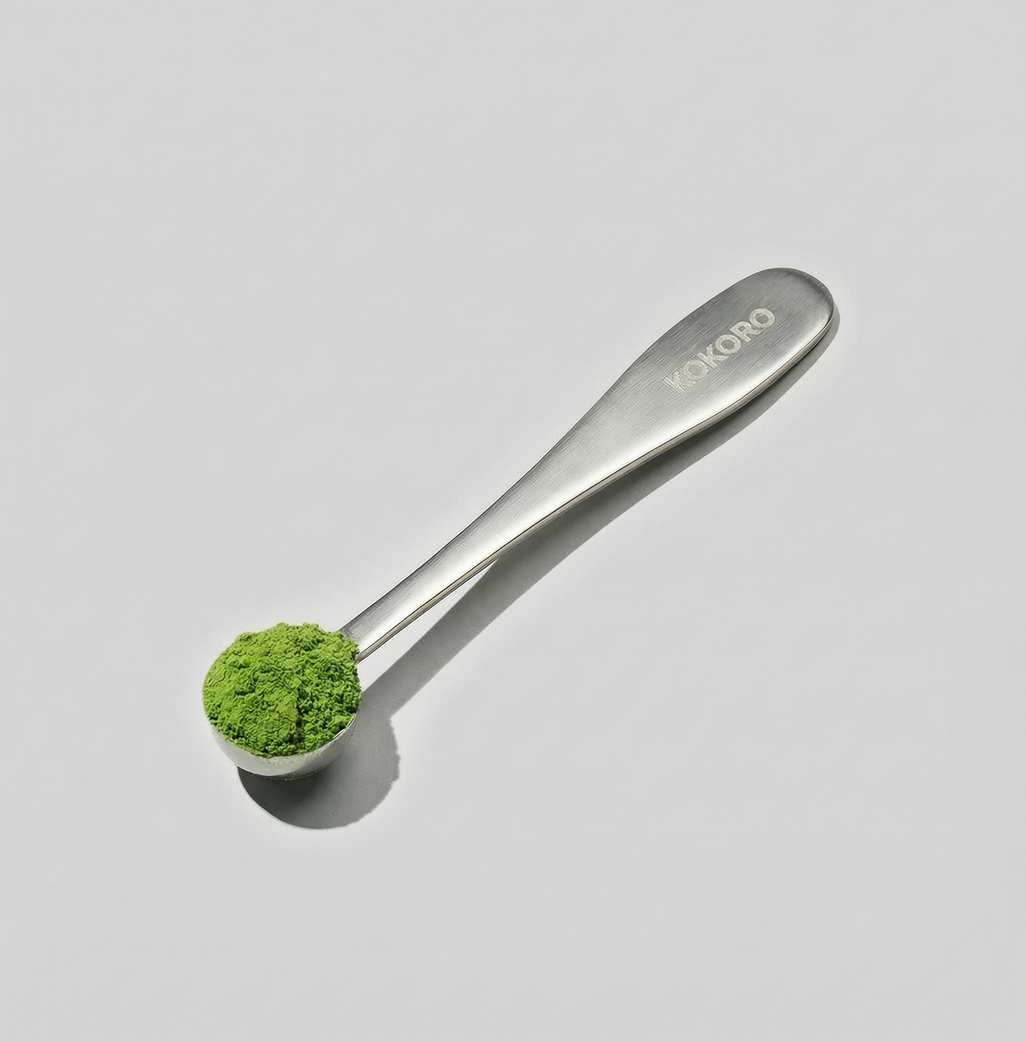 Bamboo matcha scoop (chashaku) used to measure matcha powder, photographed on a light grey background.