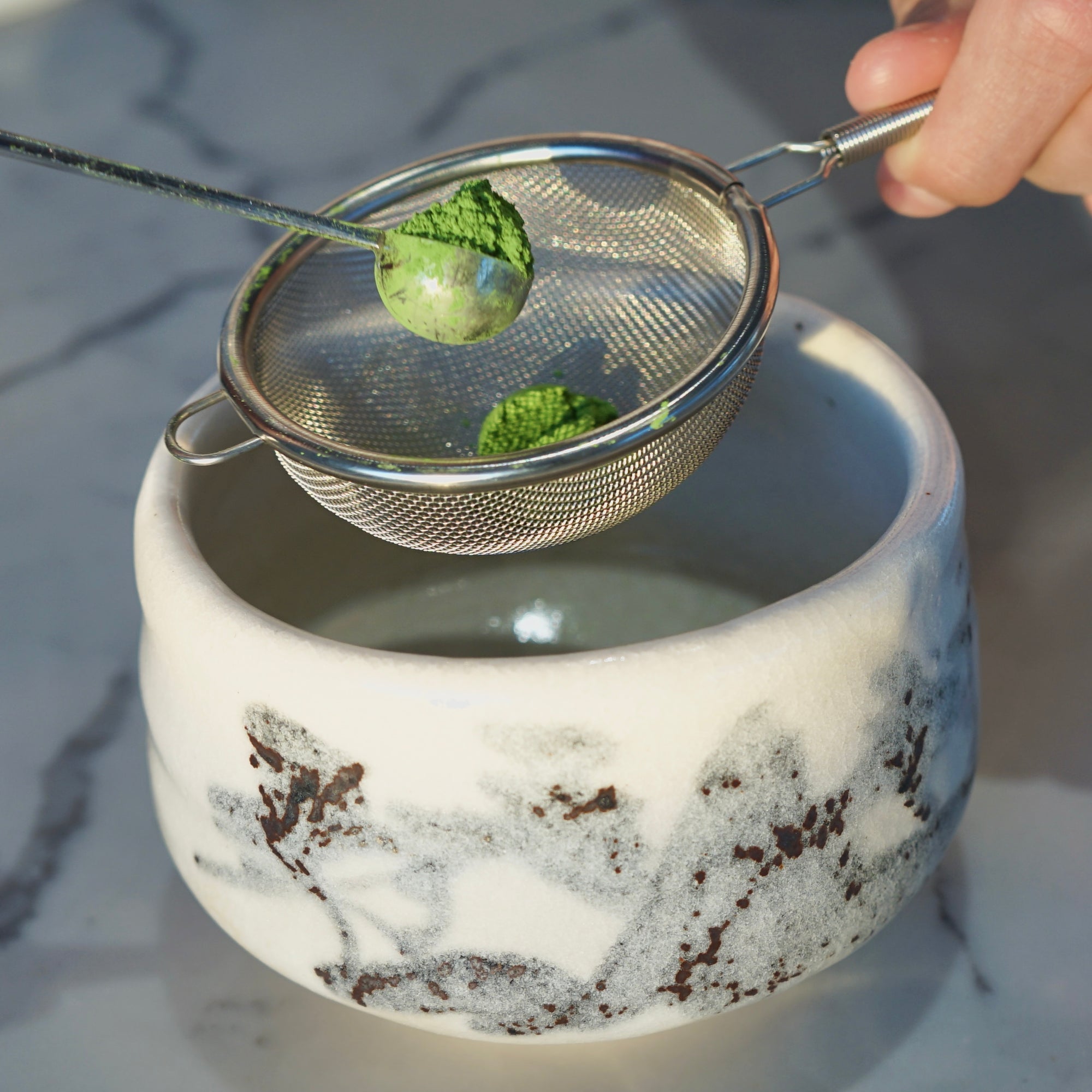 Matcha being whisked by hand with the use of a KOKORO LIFE matcha sifter and a chawan. 
