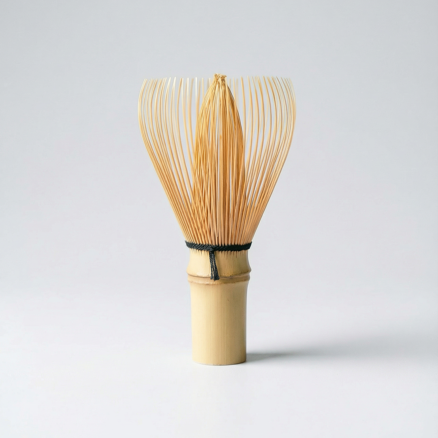 Traditional Japanese bamboo chasen for matcha preparation, photographed on a clean light grey background.